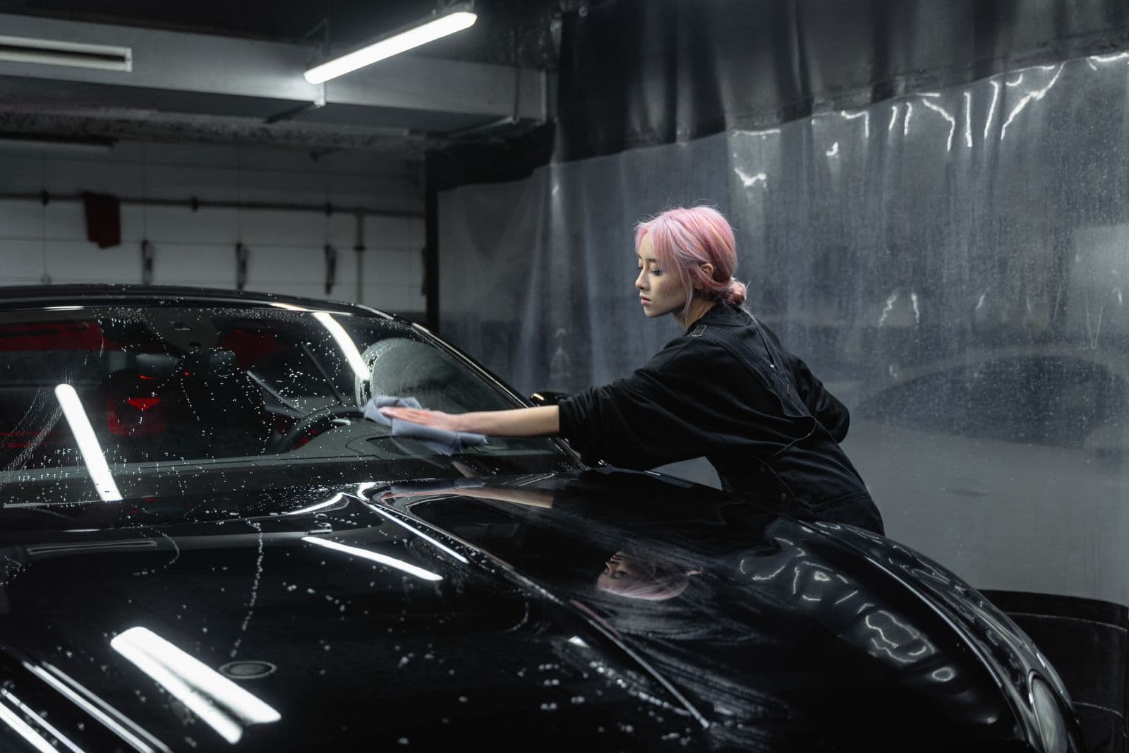 Detailer wiping a windshield with a microfiber towel in a detail bay