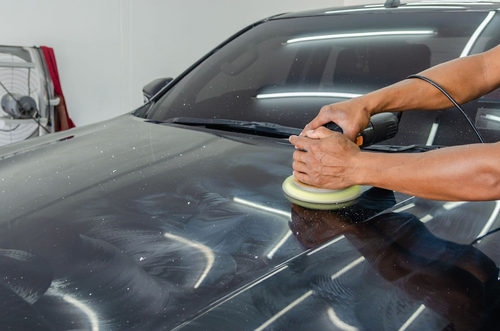 Machine polisher restoring gloss on a black hood