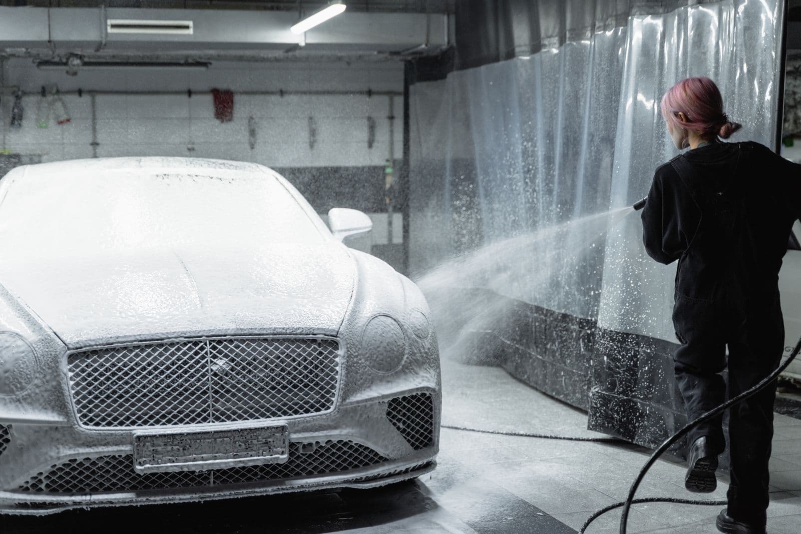 Coupe blanketed in snow foam while a detailer works the pressure washer