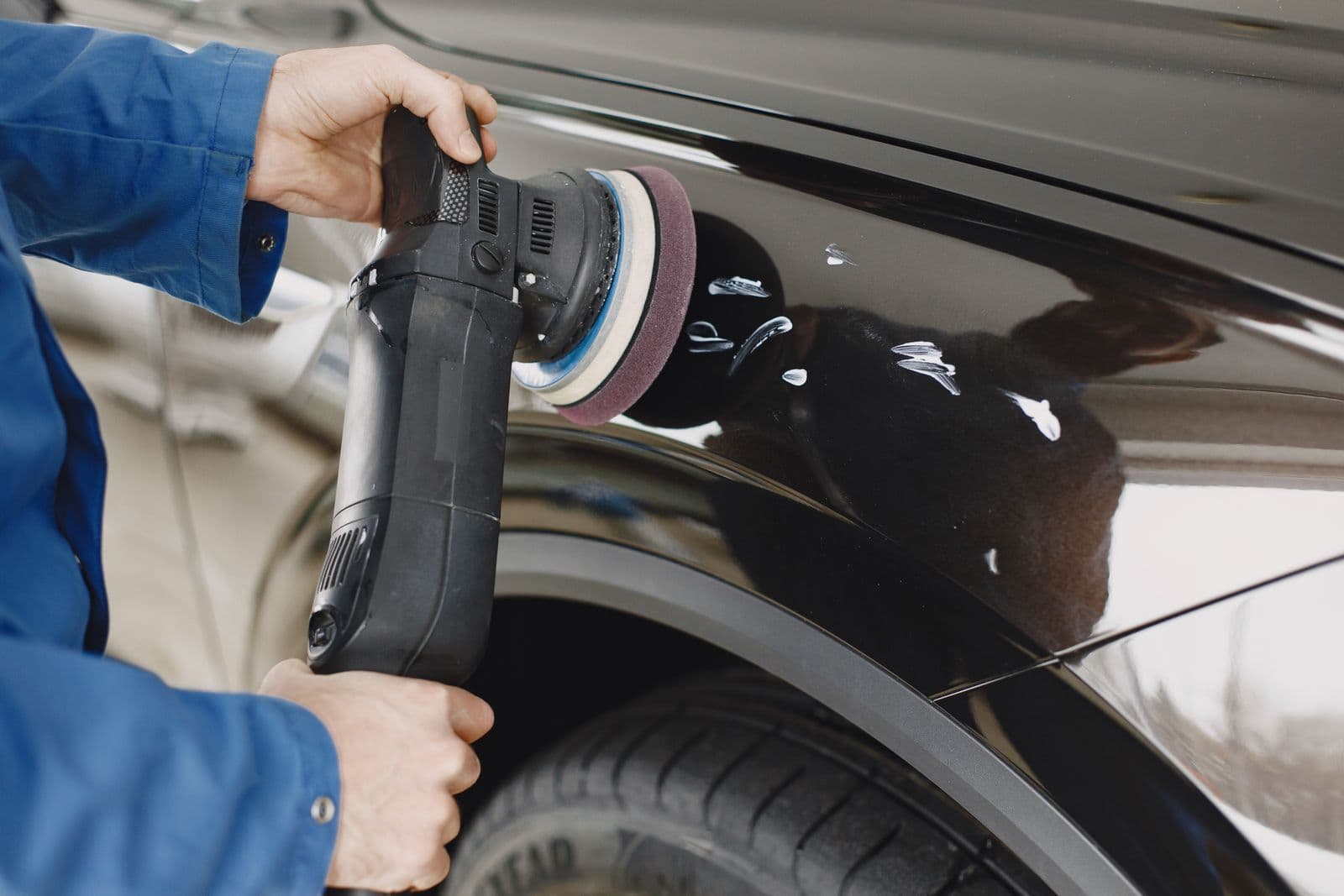 Detailer working compound into a dark fender with an orbital polisher
